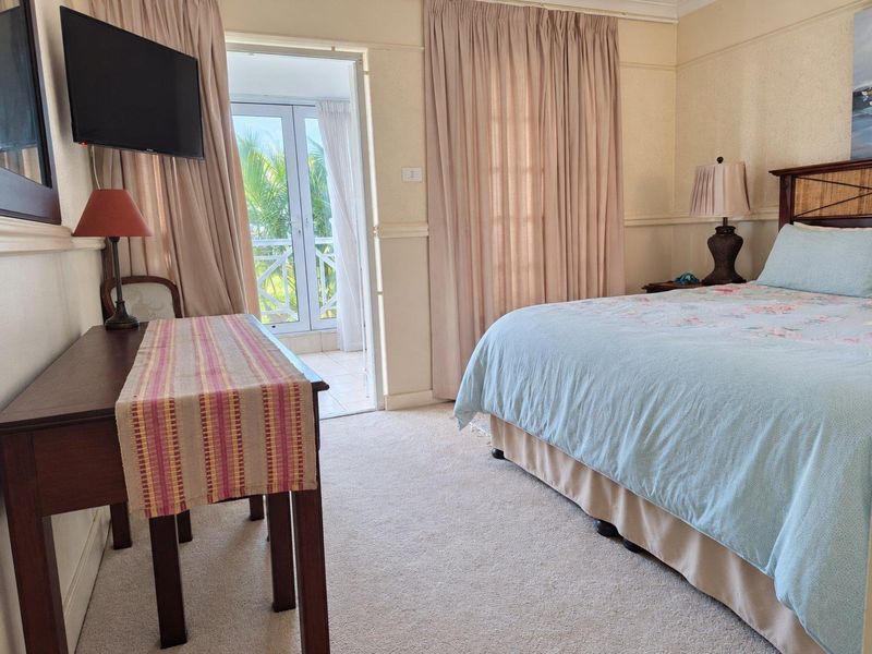 A comfortable bedroom featuring carpeted flooring, neutral wall finishes, and direct access to a private balcony through glass french doors.