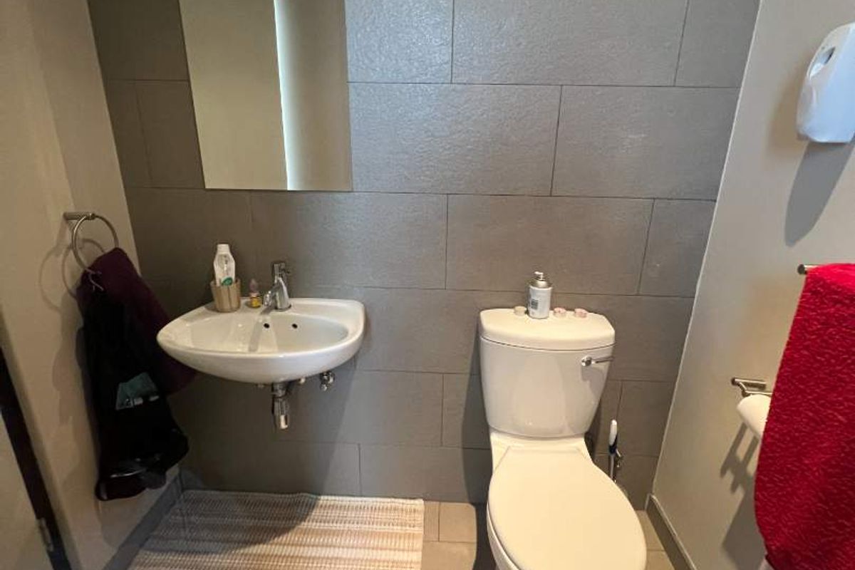 A compact bathroom featuring grey tiled walls, a wall-mounted basin, and a standard white toilet.