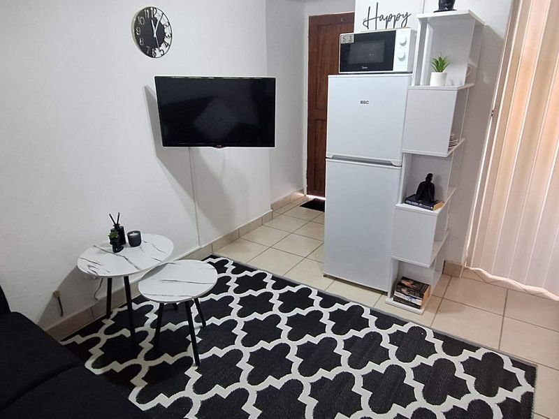 Compact open-plan living area featuring tiled flooring and a functional kitchenette with built-in cabinetry and countertop space.