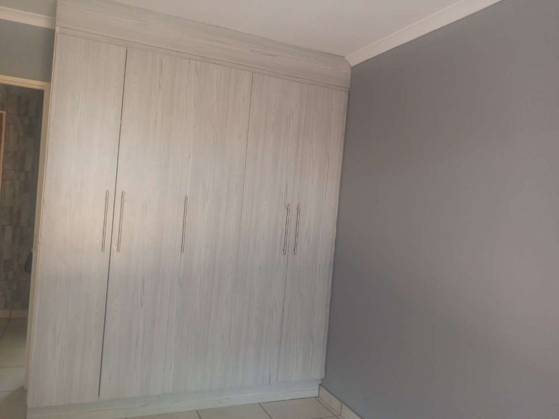 A clean, empty bedroom featuring modern light wood-grain built-in cupboards and neutral grey walls with tiled flooring.