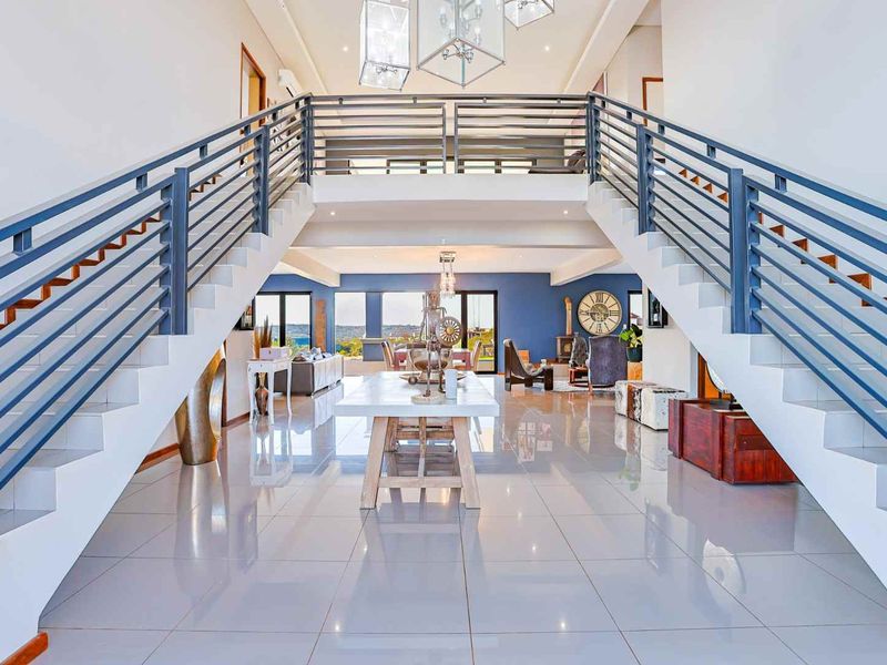 Grand double-volume entrance hall featuring a symmetrical staircase with metal balustrades, polished porcelain flooring, and an open-plan view through to the living area.