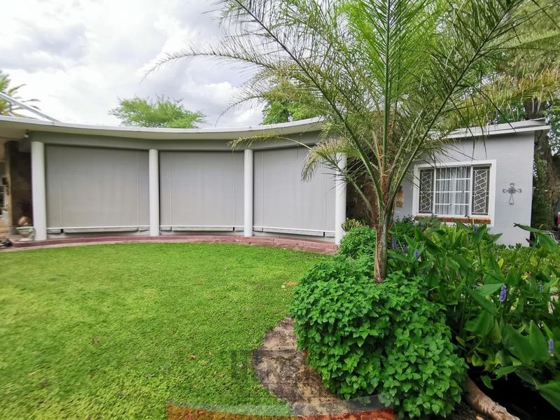 A well-maintained rear garden featuring a curved patio area with retractable outdoor blinds and established landscaping.