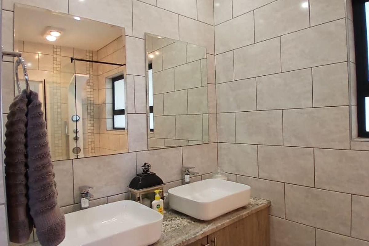 Modern bathroom featuring a double vanity with vessel sinks, granite countertop, wall-mounted cabinetry, and floor-to-ceiling tiled walls.