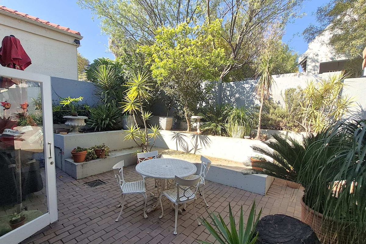 A private rear courtyard featuring brick paving, tiered concrete planter beds, and established garden landscaping, providing a quiet outdoor retreat.