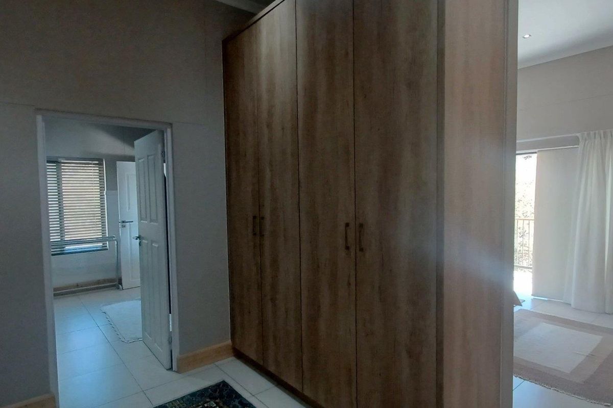 A bedroom featuring built-in wooden cupboards, tiled flooring, and an adjoining doorway leading to a secondary space.