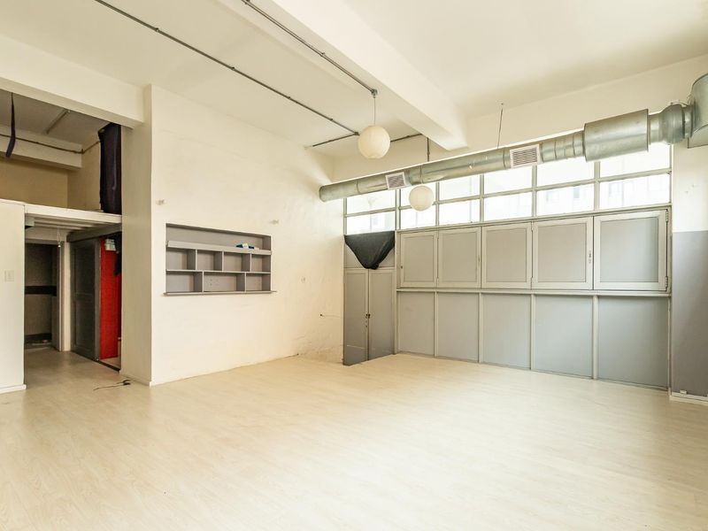 Spacious open-plan industrial style area featuring high ceilings, exposed ducting, laminate flooring, and built-in storage cabinetry.