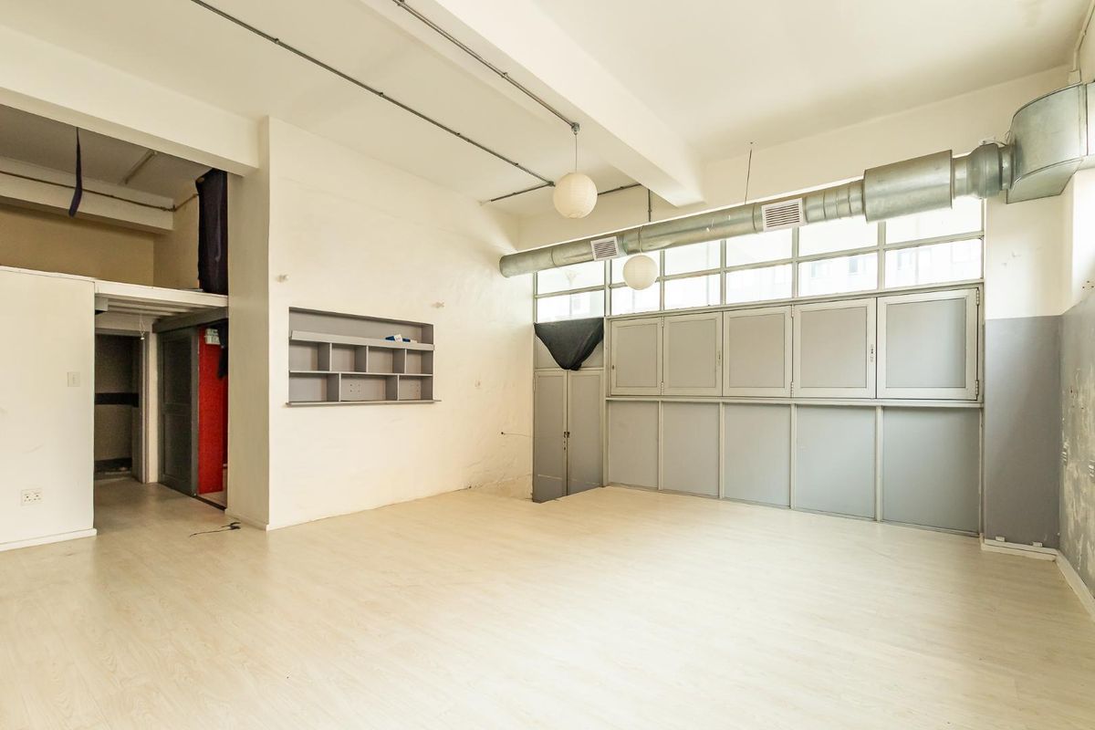 Spacious open-plan industrial style area featuring high ceilings, exposed ducting, laminate flooring, and built-in storage cabinetry.