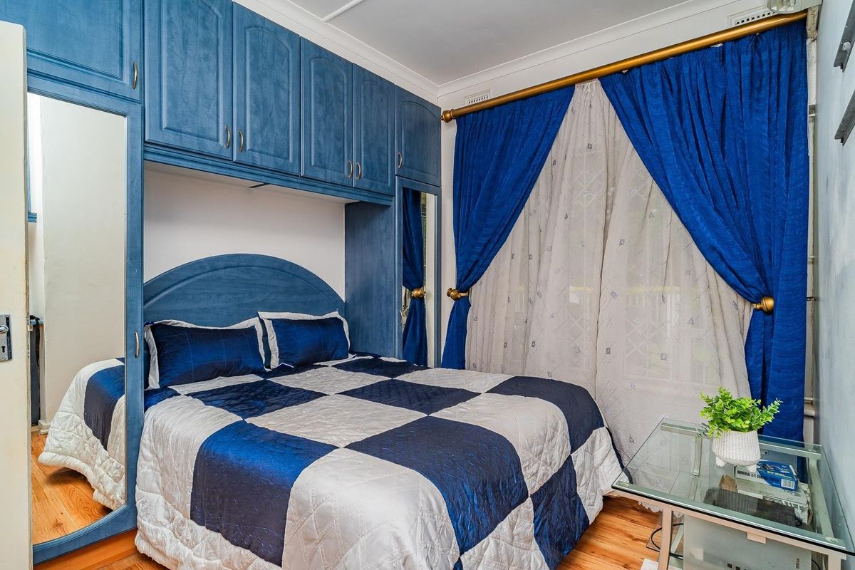 A bedroom featuring built-in blue cabinetry surrounding the bed area, timber flooring, and window treatments.