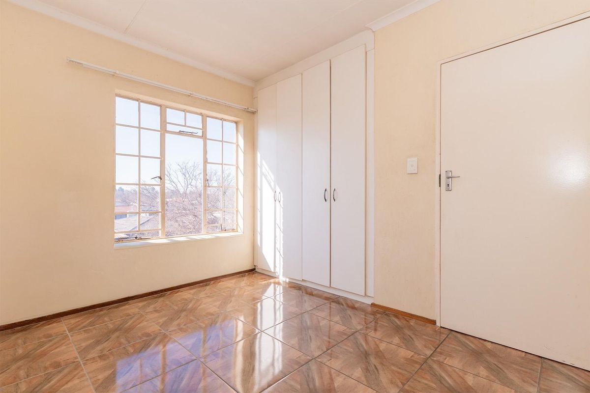 A bright, empty bedroom featuring built-in cupboards, tiled flooring, and large windows providing natural light.