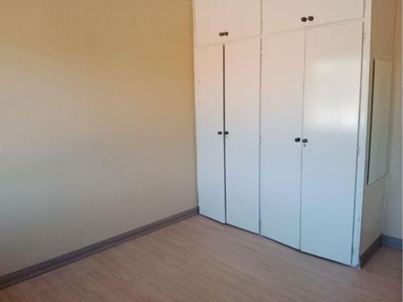 A clean, empty bedroom featuring light-toned laminate flooring and ample built-in cupboard storage with overhead cabinets.