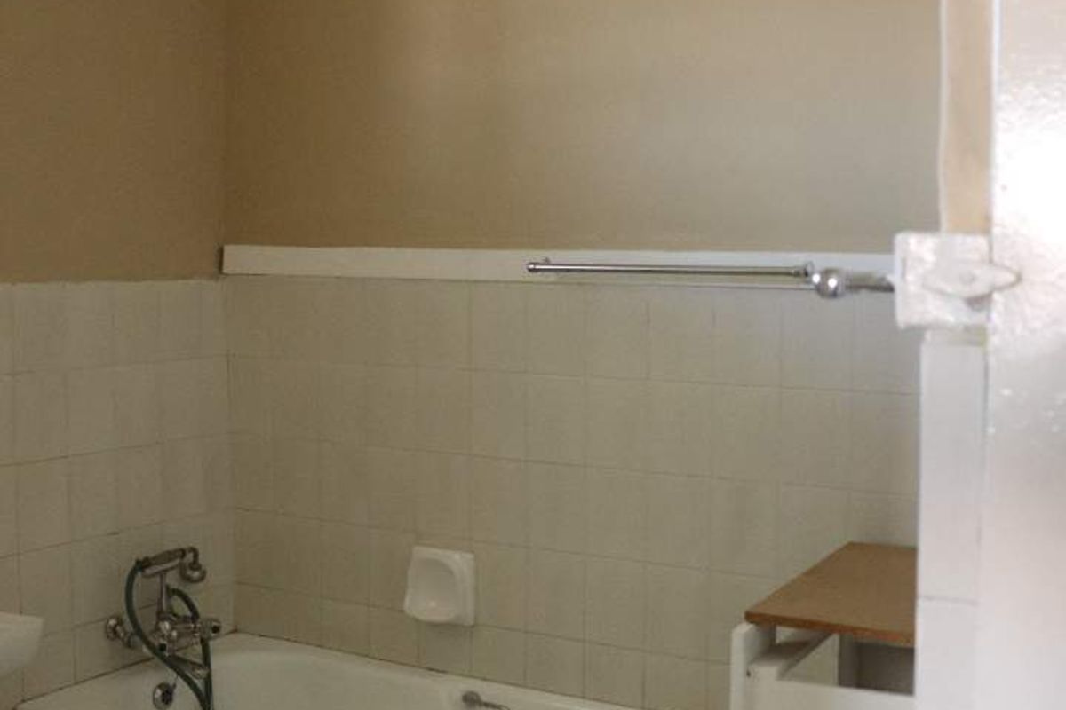 A dated bathroom featuring a built-in bathtub with tiled surround and a partially unfinished vanity area.
