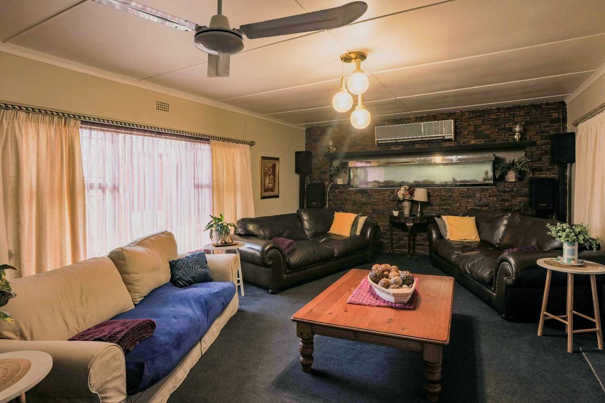 A spacious living room featuring a prominent exposed brick feature wall, ceiling fan, and wall-mounted air conditioning unit.