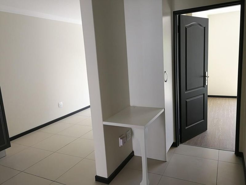 A clean, neutral hallway featuring tiled flooring, a built-in desk nook, and a dark-toned internal door leading to an adjacent room.