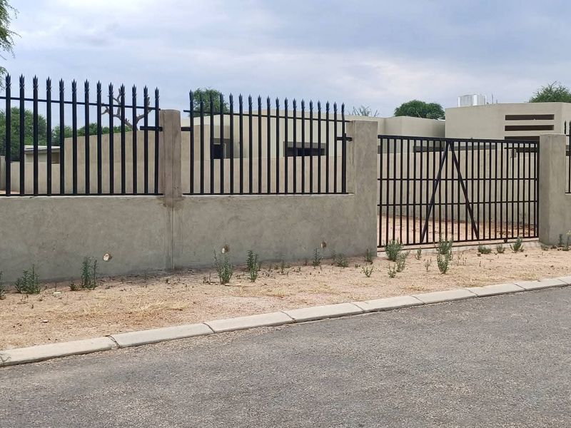 Front view of the residential property featuring a secure perimeter wall with metal fencing and a gated entrance from the paved street.