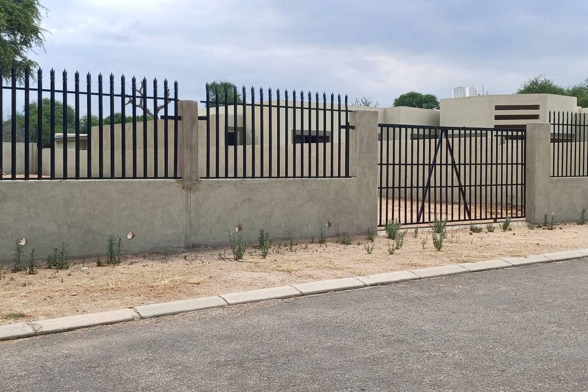 Front view of the residential property featuring a secure perimeter wall with metal fencing and a gated entrance from the paved street.