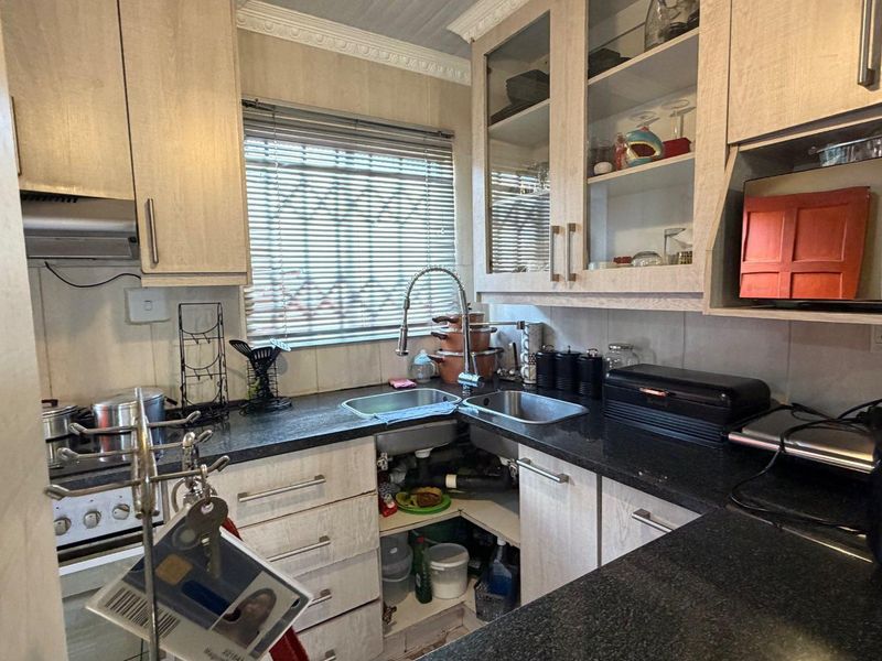 Compact kitchen featuring light wood-grain cabinetry, dark granite countertops, a double basin sink, and built-in oven with extractor fan.