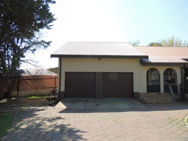 Front view of a house featuring a double garage with roller doors, a corrugated metal roof, and a paved driveway entrance.