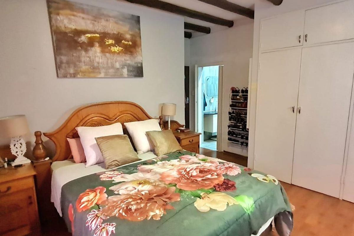 A bedroom featuring exposed ceiling beams, laminate flooring, and ample built-in cupboard storage space.