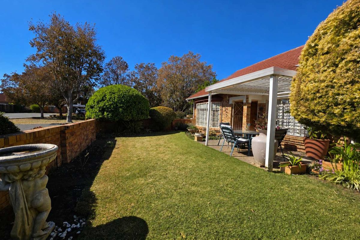 A well-maintained rear garden featuring a paved patio area with a pergola, brick boundary wall, and established lawn.