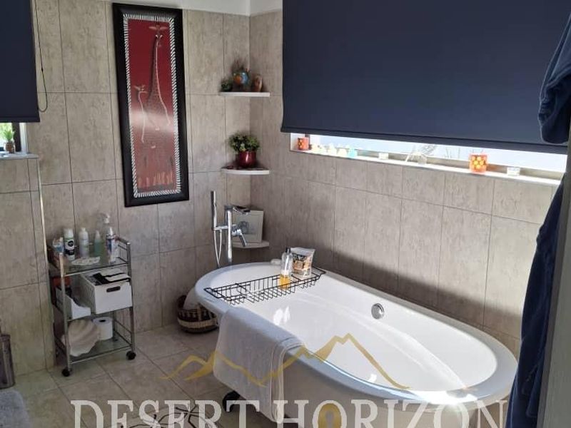 A well-maintained bathroom featuring a classic freestanding bathtub, neutral wall tiling, and modern roller blinds for privacy.