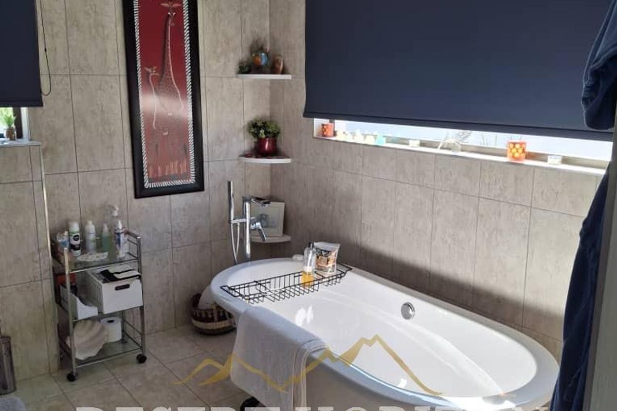 A well-maintained bathroom featuring a classic freestanding bathtub, neutral wall tiling, and modern roller blinds for privacy.