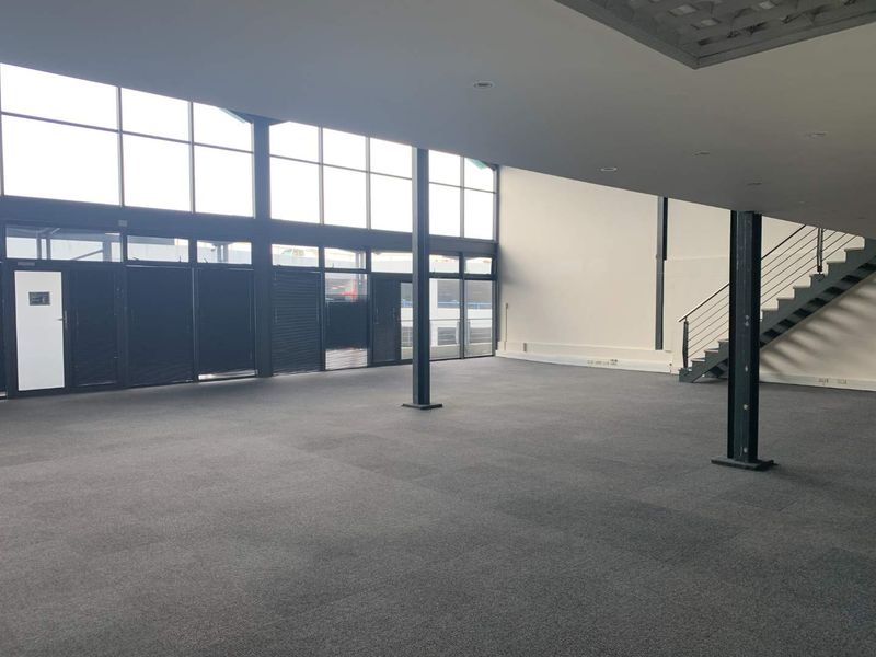 Spacious, open-plan office area featuring high ceilings, large windows for natural light, steel structural columns, and an internal staircase.