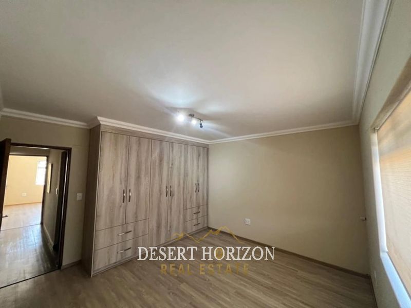 A spacious bedroom featuring modern built-in cupboards, laminate flooring, and neutral wall finishes, offering a clean and functional living space.
