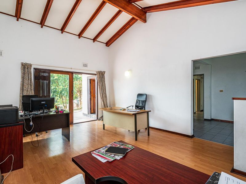Spacious home office featuring exposed timber ceiling beams, laminate flooring, and direct access to the garden through a sliding glass door.