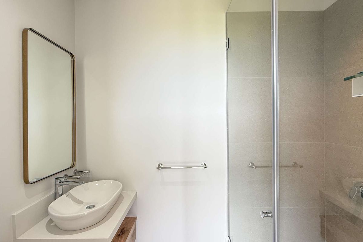Modern bathroom featuring a vessel sink vanity, wall-mounted mirror, and a glass-enclosed walk-in shower with neutral tiling.