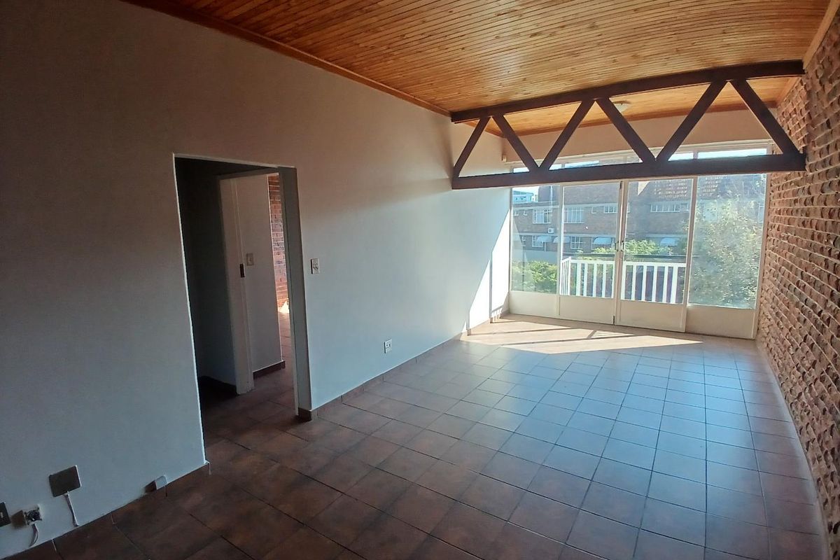 Spacious living area featuring exposed brick walls, timber-clad ceiling, and large glass sliding doors leading to a balcony.