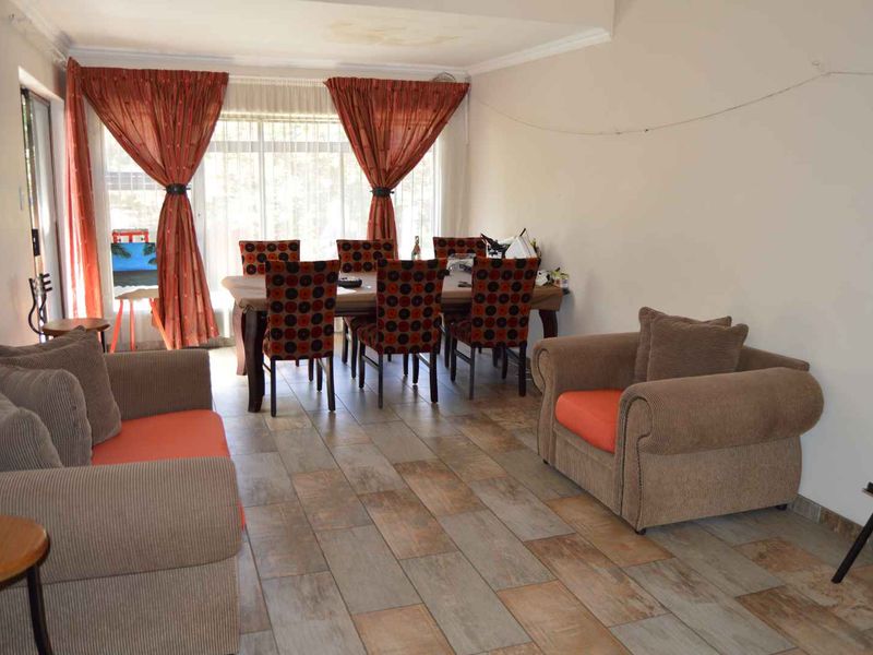 Open-plan living and dining area featuring tiled flooring, large windows, and sliding door access, showing signs of ceiling water damage and wall wear.