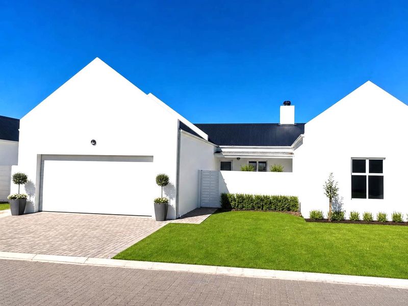 Modern single-story house exterior featuring a clean white facade, dark metal roof, paved driveway, and well-maintained front lawn.