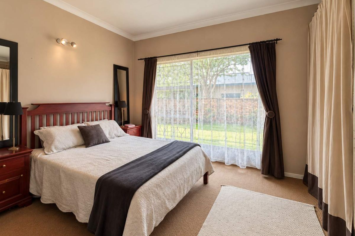 A well-lit bedroom featuring carpeted flooring, cove cornicing, and a large sliding glass door with security gate providing access to the garden.