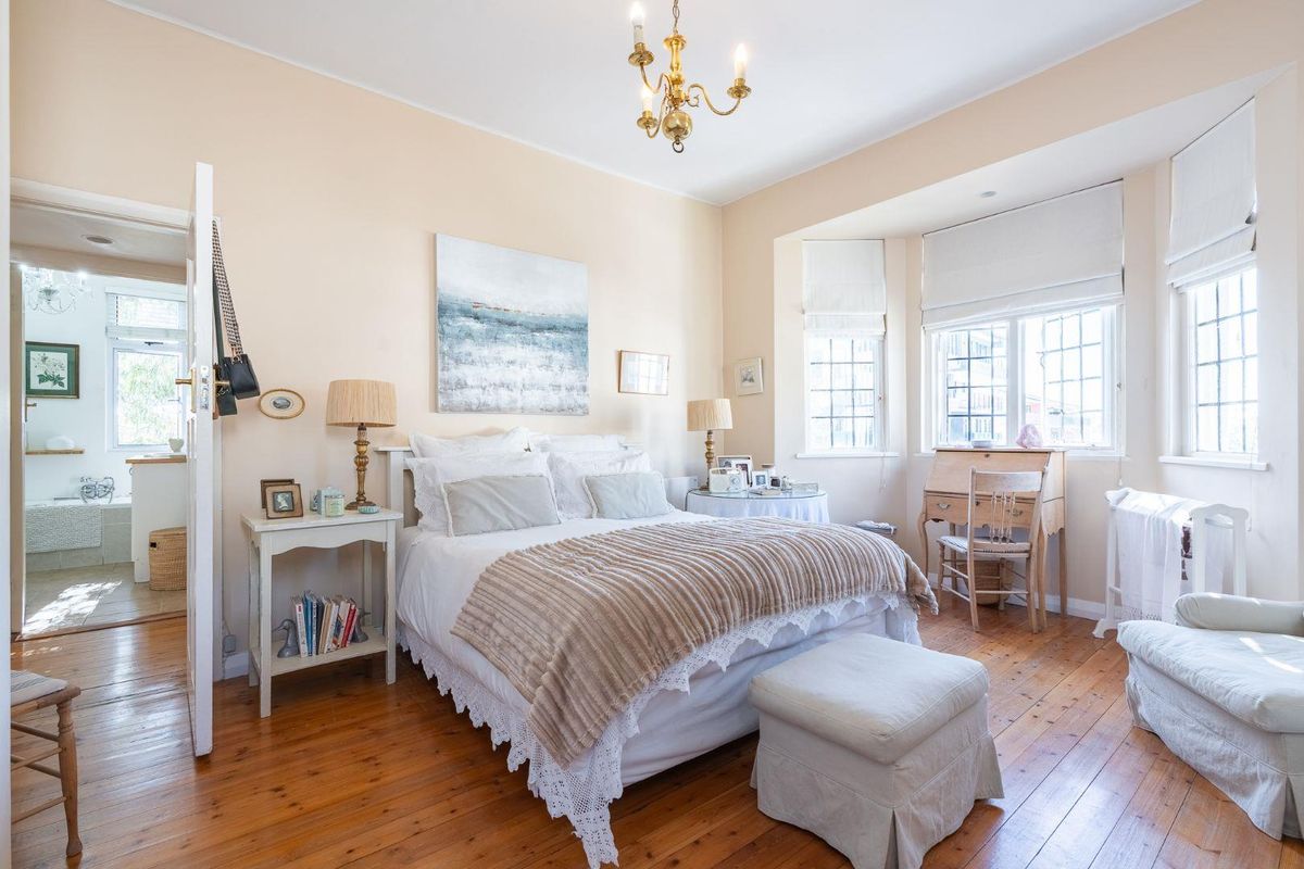 A bright and spacious bedroom featuring polished hardwood flooring, a classic bay window, and direct access to an adjoining en-suite bathroom.