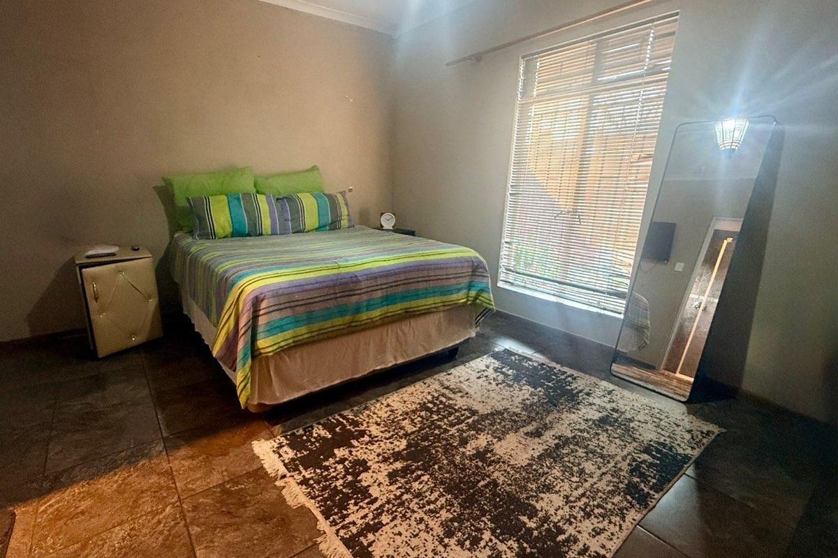 A bedroom featuring tiled flooring, a large window with fitted blinds, and neutral wall finishes.