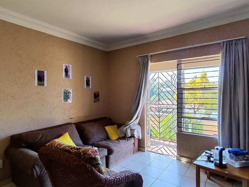 A living room featuring tiled flooring, coving, and a sliding door leading to a balcony with security bars and a gate.