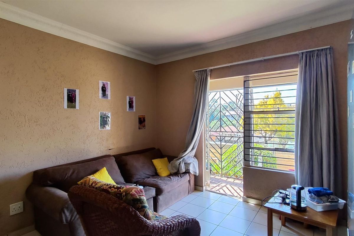 A living room featuring tiled flooring, coving, and a sliding door leading to a balcony with security bars and a gate.