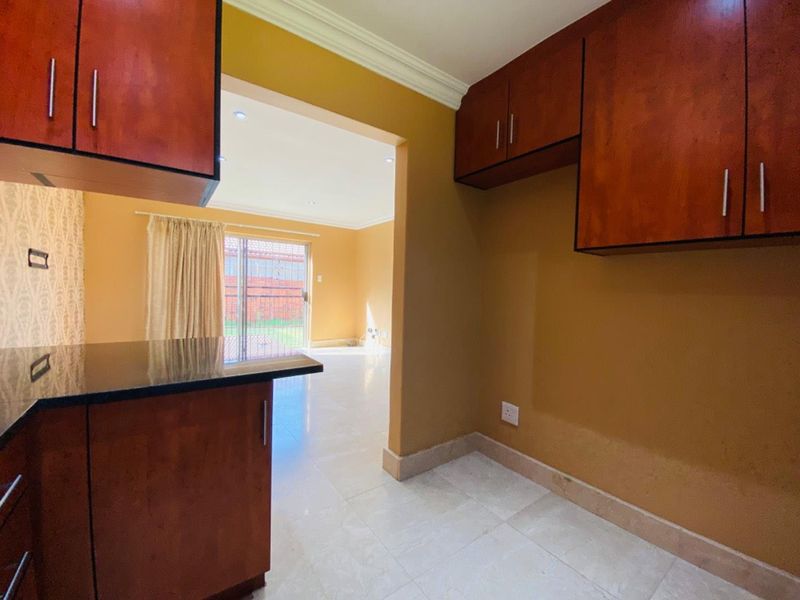 A functional kitchen area featuring built-in wooden cabinetry, granite countertops, and tiled flooring, with an open-plan flow leading to the living space.