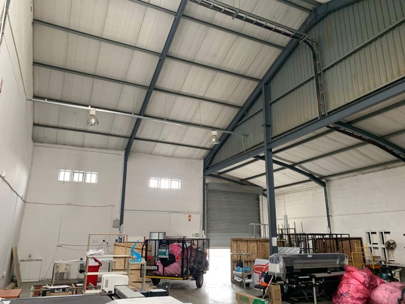 Spacious industrial warehouse unit featuring high ceilings, exposed steel structural beams, concrete flooring, and a large roller shutter door for vehicle access.