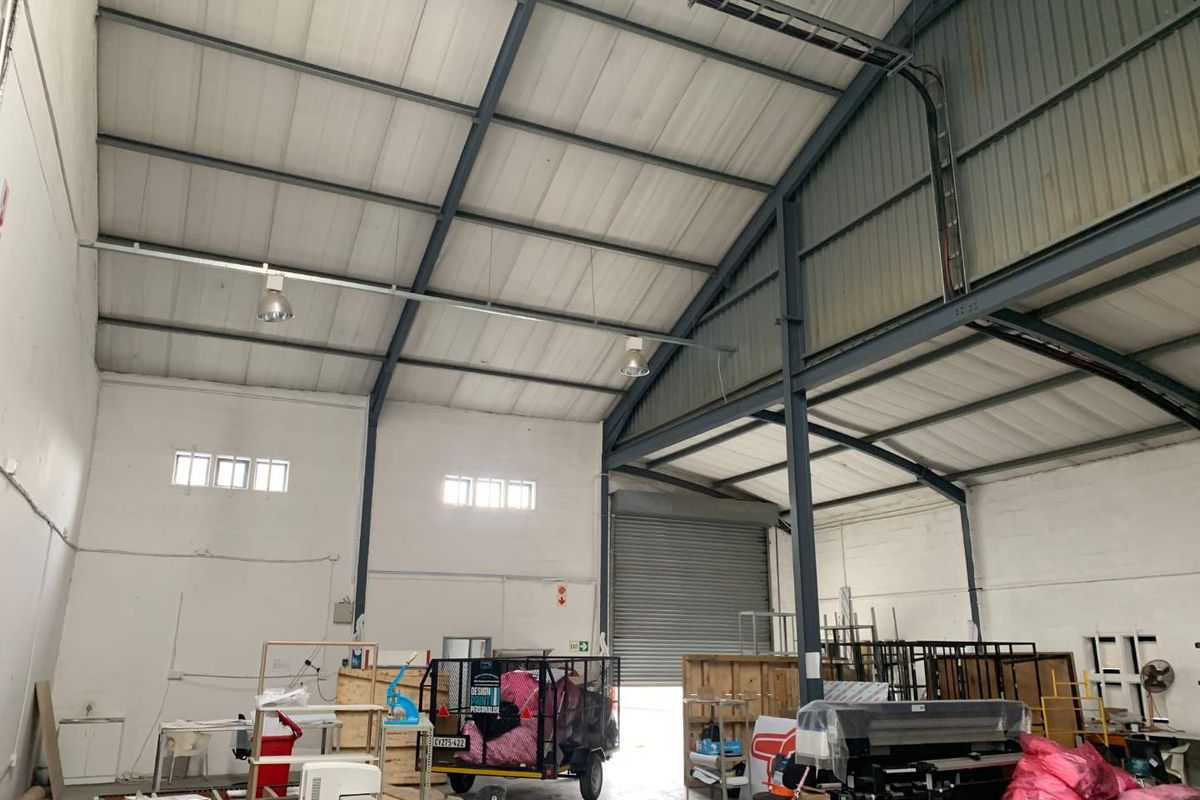 Spacious industrial warehouse unit featuring high ceilings, exposed steel structural beams, concrete flooring, and a large roller shutter door for vehicle access.