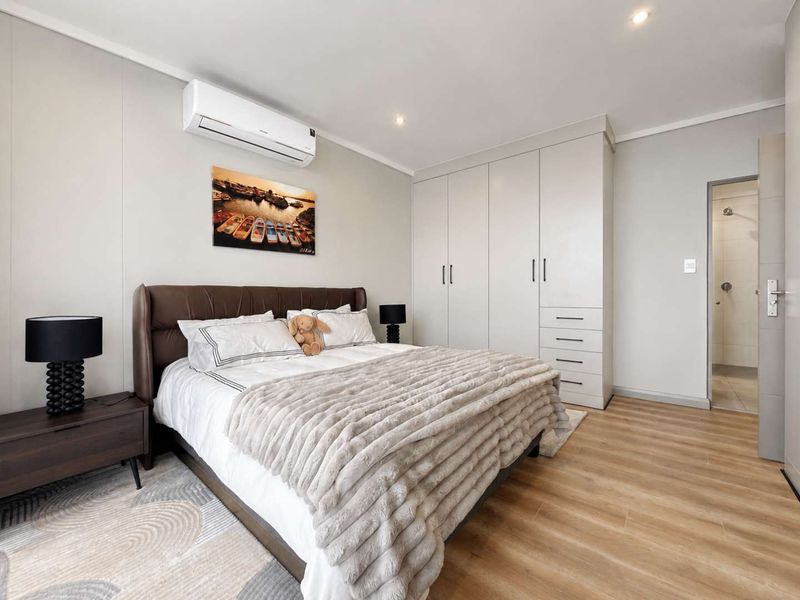 A well-maintained bedroom featuring laminate flooring, built-in cupboards, an air conditioning unit, and direct access to an en-suite bathroom.
