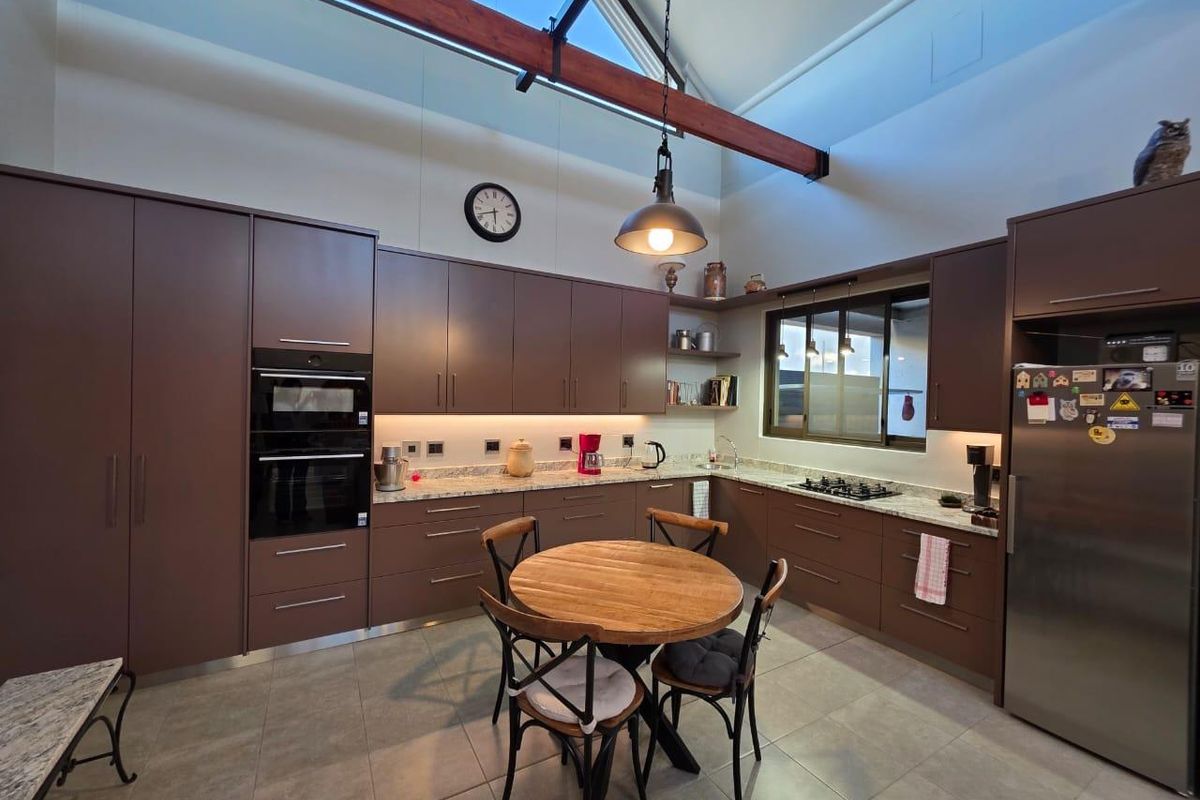Modern kitchen featuring dark cabinetry, stone countertops, built-in double oven, gas hob, and high vaulted ceilings with exposed timber beams.
