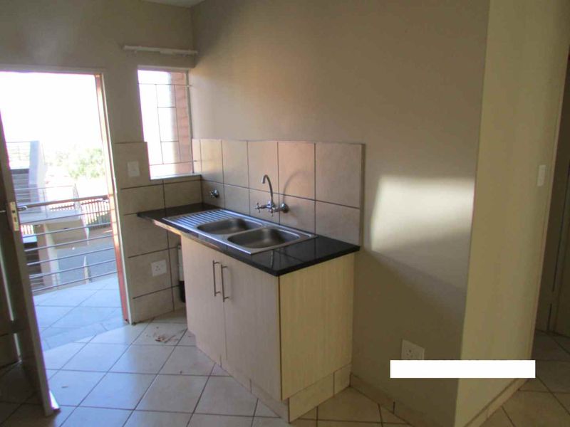 A compact kitchen area featuring a stainless steel double sink, granite countertop, tiled backsplash, and light-toned cabinetry, with direct access to an outdoor balcony.