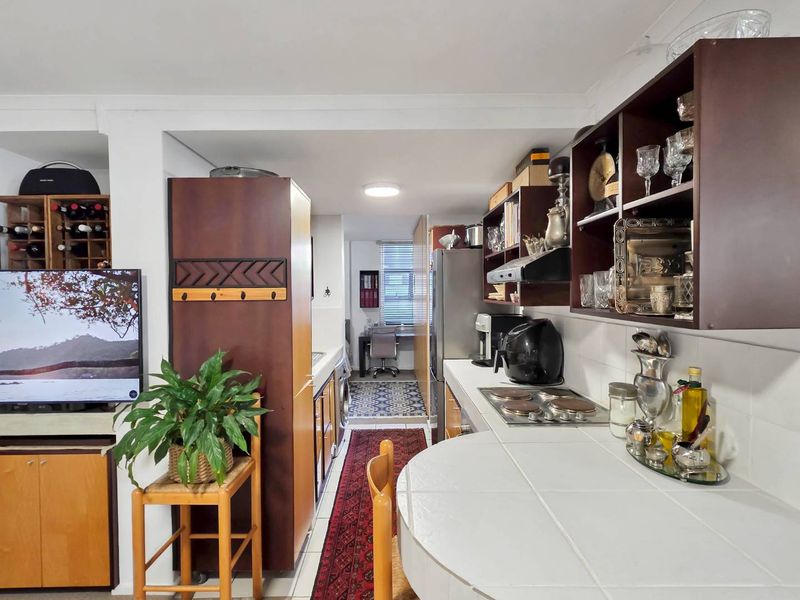 Open-plan kitchen area featuring dark wood cabinetry, tiled countertops, integrated hob, and a built-in wine rack, flowing into a secondary utility or office space.