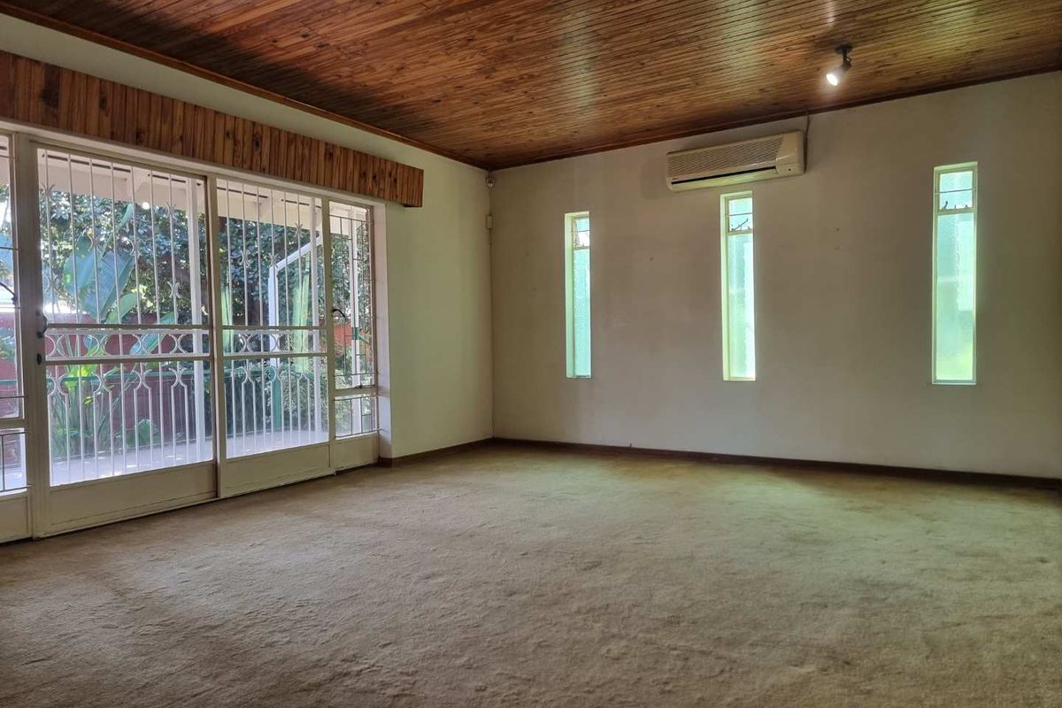 Spacious living area featuring a timber-paneled ceiling, wall-mounted air conditioning unit, and large sliding glass doors with security gates leading to the patio.
