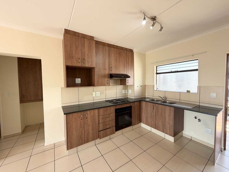 A clean, functional kitchen featuring wood-look cabinetry, granite countertops, built-in oven, hob, extractor fan, and a double bowl sink with tiled flooring.