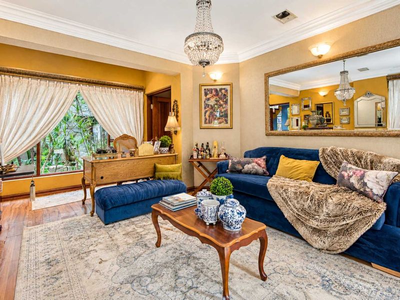 A well-maintained living room featuring hardwood flooring, crown molding, a crystal chandelier, and a large wall mirror, offering a classic and elegant aesthetic.