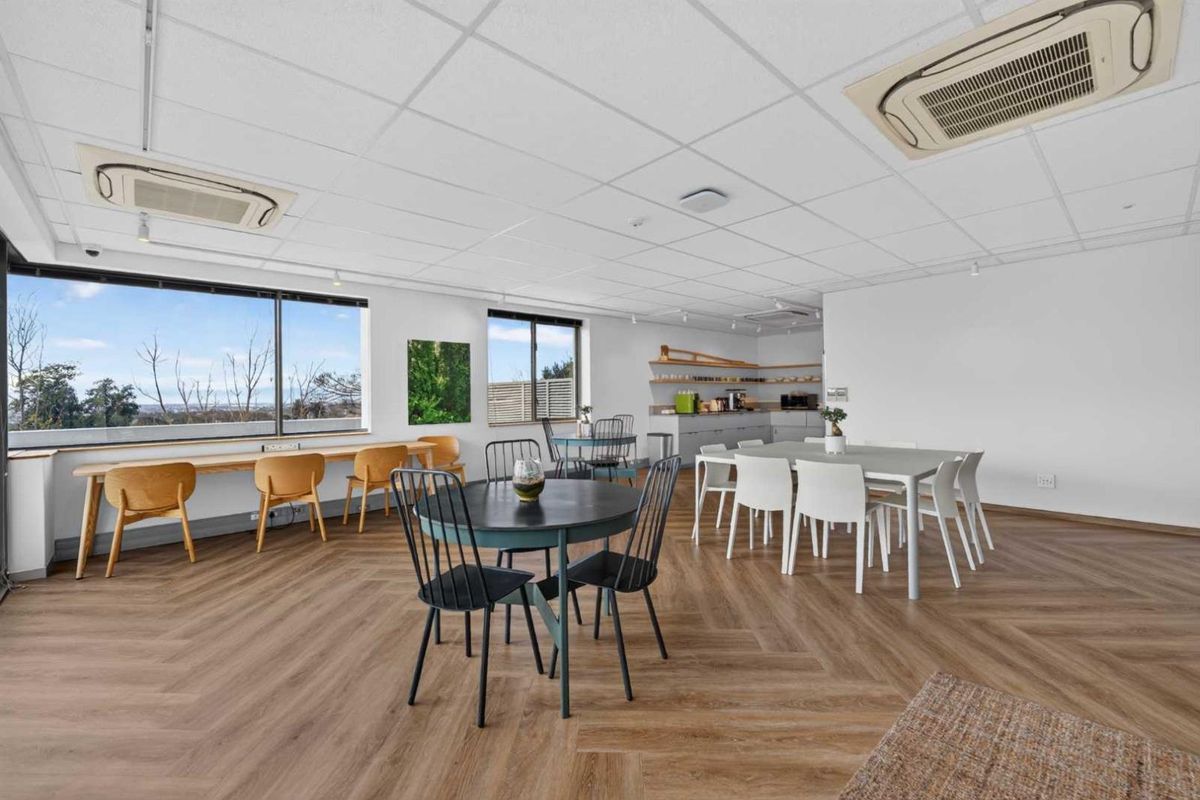 Spacious open-plan office area featuring herringbone wood-look flooring, recessed ceiling air conditioning units, and large windows providing ample natural light.