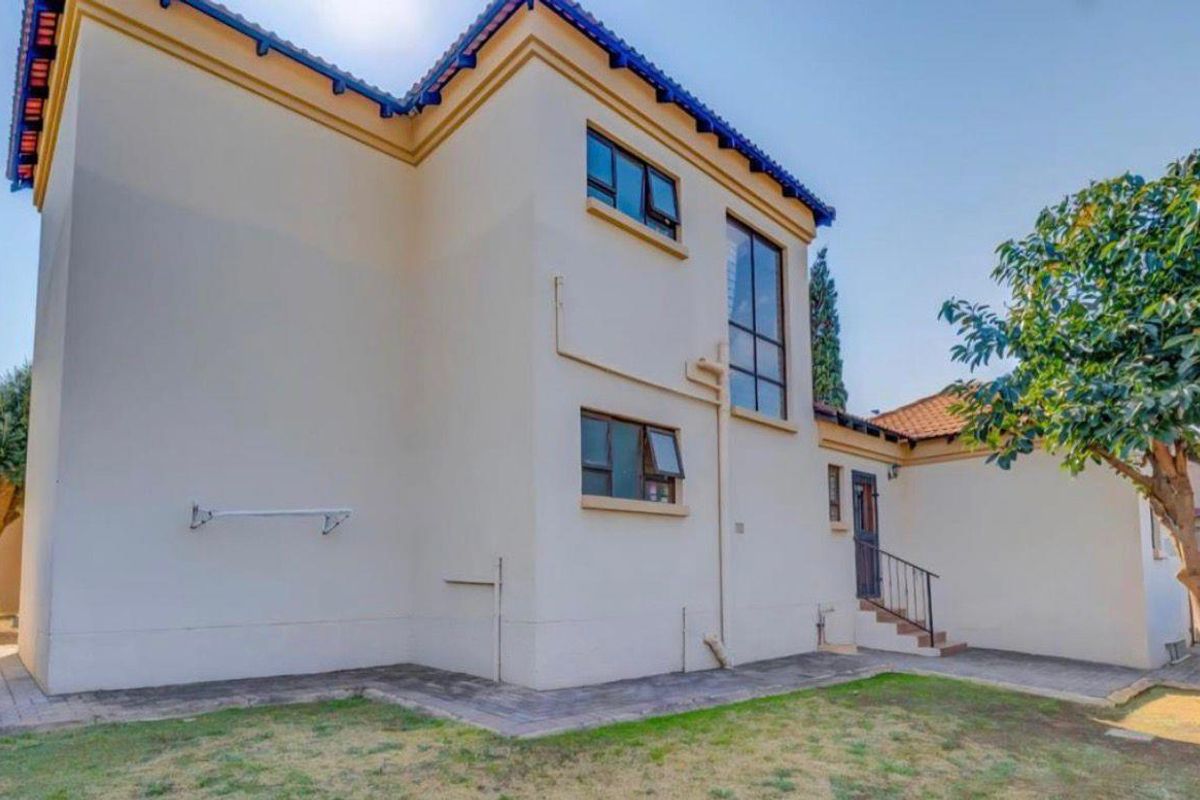 A view of the rear exterior elevation featuring a two-story structure, paved walkway, and access steps leading to a side entrance.