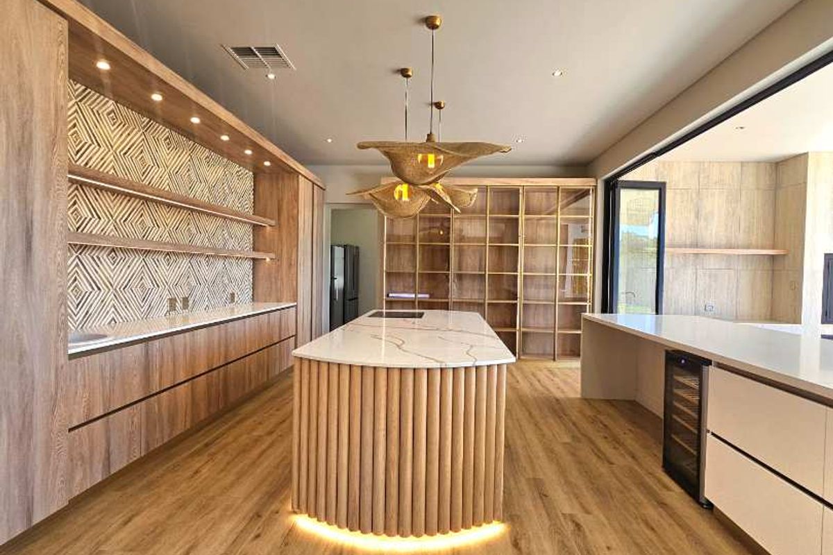 Modern kitchen featuring a central island with integrated lighting, custom wood cabinetry, stone countertops, and built-in wine cooler, offering a sleek, high-end aesthetic.
